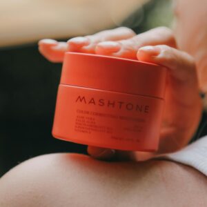 Close-up of a woman holding a Mashtone moisturizing cream jar with blurred background.