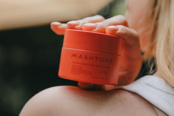 Close-up of a woman holding a Mashtone moisturizing cream jar with blurred background.