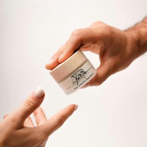 Close-up of hands exchanging a jar of luxury skincare cream on a white background.