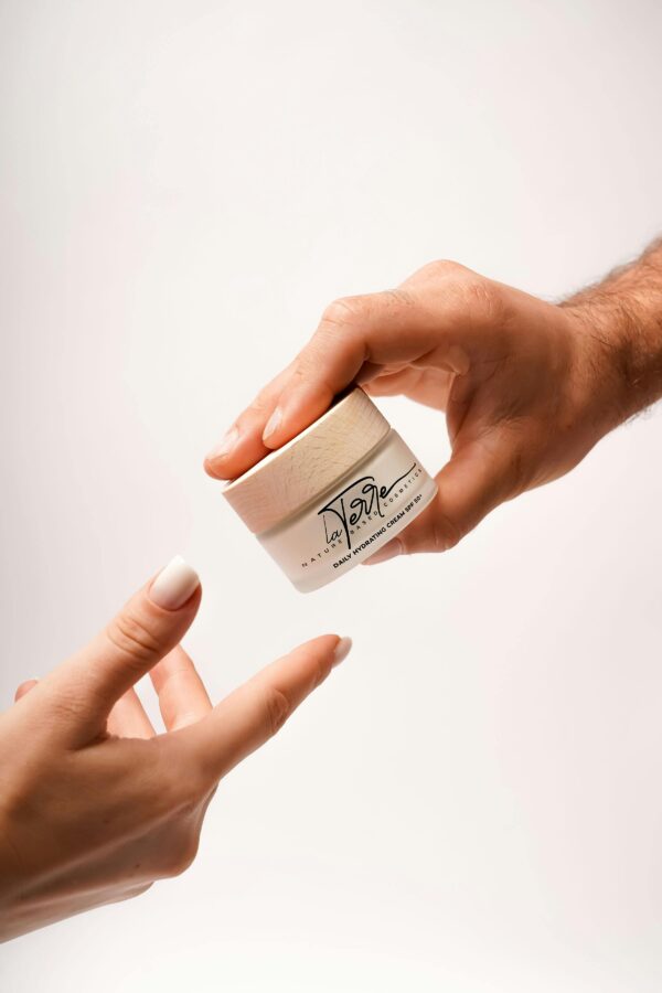 Close-up of hands exchanging a jar of luxury skincare cream on a white background.