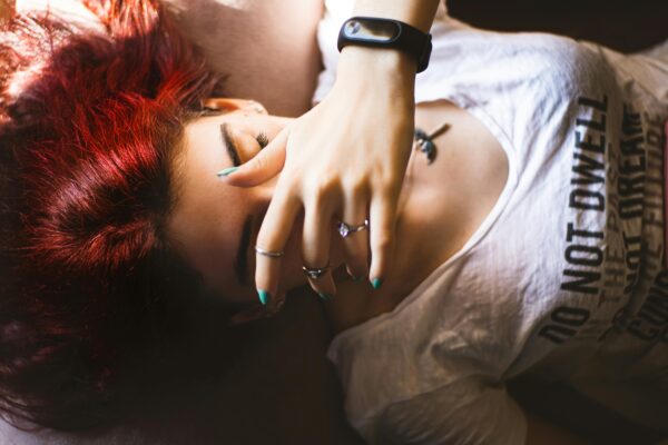 Young woman with red hair resting indoors, wearing rings and a smartwatch.