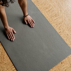 Close-up of hands on a grey yoga mat on a wooden floor, from above.