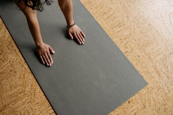 Close-up of hands on a grey yoga mat on a wooden floor, from above.