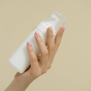 A close-up of a hand holding a white cosmetic bottle against a neutral background, perfect for product mockups and beauty industry use.