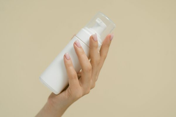 A close-up of a hand holding a white cosmetic bottle against a neutral background, perfect for product mockups and beauty industry use.